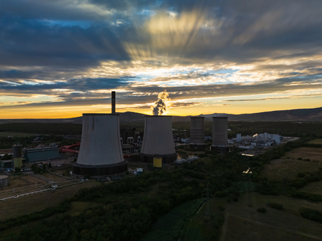 Aerial view of the lignite fired Matra power plant with cooling towers and steam at sunset in Visonta Hungary surrounded by rural fields and the Matra hills.