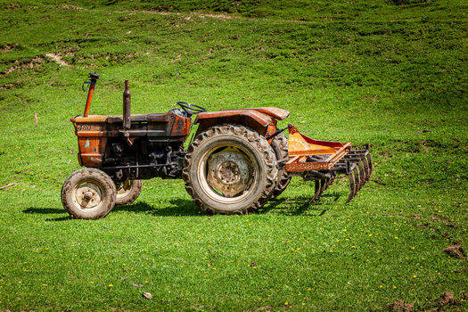 View of an orange tractor with a plow attachment parked on a lush green grassy hillside in Arang Kel Azad Kashmir Pakistan. View of an orange tractor with a plow attachment parked on a lush green grassy hillside in Arang Kel Azad Kashmir Pakistan.