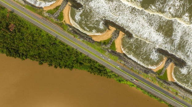 Aerial view of Maravanthe beach showing the narrow land strip between the Arabian Sea and Souparnika River with a coastal road running parallel to the shore in Maravanthe Karnataka India. Aerial view of Maravanthe beach showing the narrow land strip between the Arabian Sea and Souparnika River with a coastal road running parallel to the shore in Maravanthe Karnataka India.