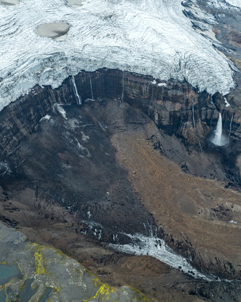 Aerial view of the Langjokull glacier edge featuring dark volcanic rock formations cascading waterfalls and melting ice in Vik Myrdalshreppur Iceland.