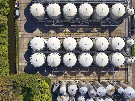 Aerial view of rows of large white food oil and fat storage tanks at an industrial facility next to a canal and green trees in Wormer North Holland Netherlands.