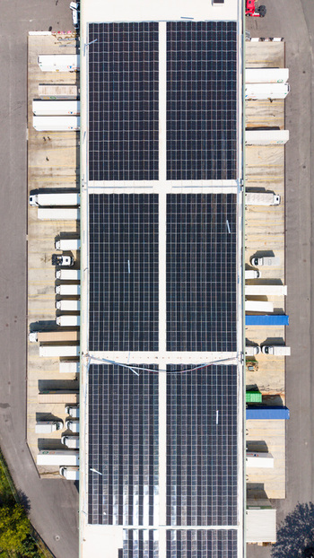 Aerial view of a logistics hub featuring extensive rooftop solar panels numerous parked semi trucks and loading docks for distribution operations in Melegnano Lombardy Italy.