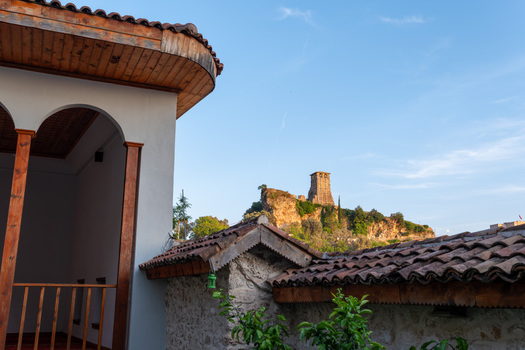 View of the historic Kruje Castle clock tower on a rocky hill seen from a traditional building with tiled roofs and wooden arches in Kruje Durres County Albania.