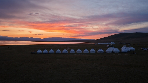 Aerial view of Song Kul lake featuring a traditional yurt camp on the grassy plains under a vibrant sunset sky in Naryn Region Kyrgyzstan. Aerial view of Song Kul lake featuring a traditional yurt camp on the grassy plains under a vibrant sunset sky in Naryn Region Kyrgyzstan.