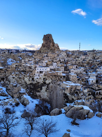 View of the historic stone houses and rock formations of Cappadocia featuring Uchisar Castle covered in snow under a clear blue sky in Turkiye. View of the historic stone houses and rock formations of Cappadocia featuring Uchisar Castle covered in snow under a clear blue sky in Turkiye.