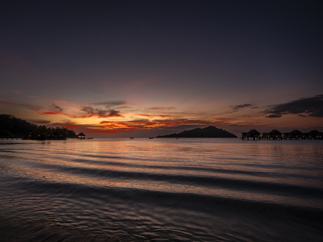 View of Likuliku Lagoon Resort at sunset with overwater bungalows silhouetted against a vibrant orange and purple sky over the calm ocean in Yaro Nadroga Navosa Fiji.
