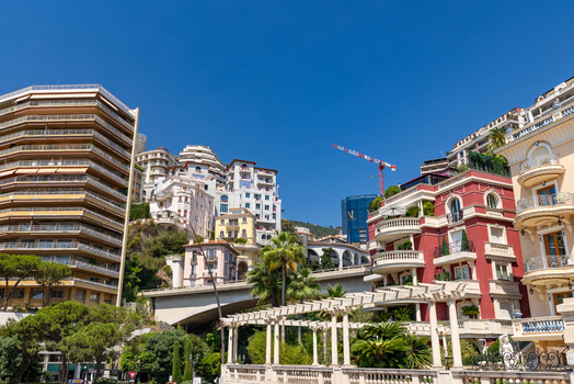 View of the urban landscape of Monaco City with its Mediterranean architecture terraced buildings palm trees and a construction crane against a clear blue sky in Monaco City Monaco. View of the urban landscape of Monaco City with its Mediterranean architecture terraced buildings palm trees and a construction crane against a clear blue sky in Monaco City Monaco.