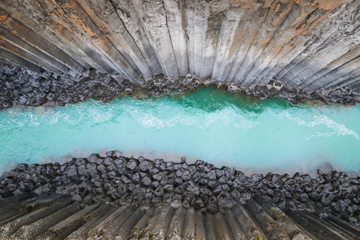 Aerial view of the turquoise glacial river flowing through the towering basalt columns of Studlagil Canyon in Eiriksstadhir Mulathing Iceland. Aerial view of the turquoise glacial river flowing through the towering basalt columns of Studlagil Canyon in Eiriksstadhir Mulathing Iceland.