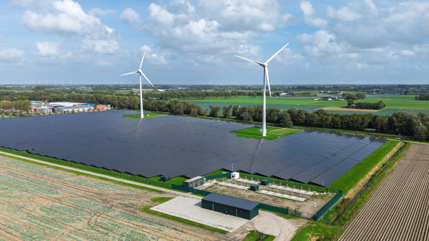 Aerial view of a large solar farm with two wind turbines surrounded by green agricultural fields in Warmenhuizen North Holland Netherlands.