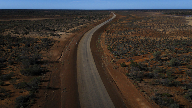Aerial view of an asphalt road stretching through the arid red earth landscape of the Australian outback under a clear blue sky in Perth Western Australia Australia.