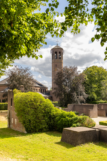 View of the historic church tower rising above brick ruins and lush green trees in a park setting in Heusden North Brabant Netherlands.