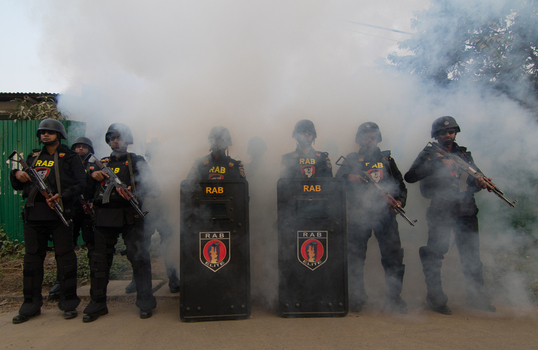 Dhaka Bangladesh 01 February 2017 View of Rapid Action Battalion RAB officers in black uniforms and gear standing with riot shields and rifles amidst thick smoke. Dhaka Bangladesh 01 February 2017 View of Rapid Action Battalion RAB officers in black uniforms and gear standing with riot shields and rifles amidst thick smoke.