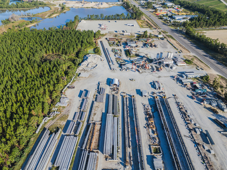Aerial view of an industrial concrete bridge manufacturing facility with rows of steel I beams heavy machinery and storage yards in Wilmington North Carolina United States. Aerial view of an industrial concrete bridge manufacturing facility with rows of steel I beams heavy machinery and storage yards in Wilmington North Carolina United States.