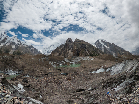 View of Baltoro Glacier with rugged rocky terrain glacial meltwater pools and towering snow capped mountain peaks under a cloudy sky in Baltoro Gilgit Baltistan Pakistan.