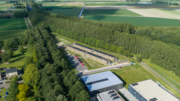Aerial view of a modern residential building complex surrounded by lush green trees and agricultural fields in Middenmeer North Holland Netherlands.