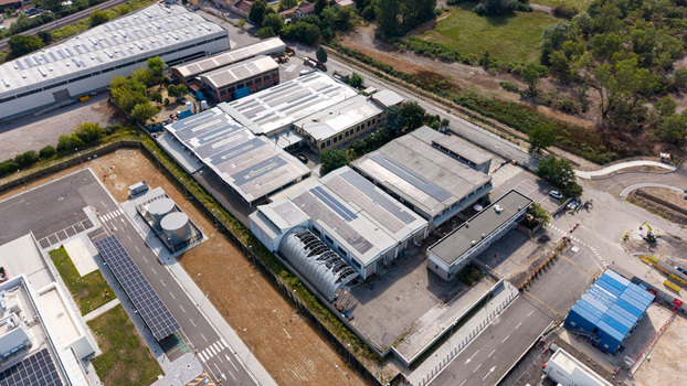 Aerial view of an industrial manufacturing and warehouse complex featuring extensive rooftop solar panels highlighting sustainable energy integration in Melegnano Lombardy Italy.