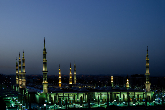 View of Al Masjid e Nabawi illuminated at night with its iconic minarets and domes glowing against the dark blue sky in Madinah Al Madinah Province Saudi Arabia.