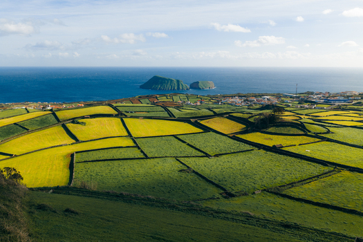 Aerial view of the patchwork fields near Pico Dona Joana divided by stone walls overlooking the ocean and coastal village Feteira Acores Portugal.