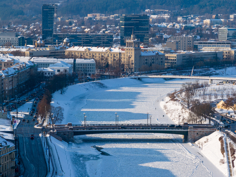Aerial view of the frozen Neris River and the Green Bridge surrounded by snow covered banks and urban architecture in Vilnius County Lithuania.