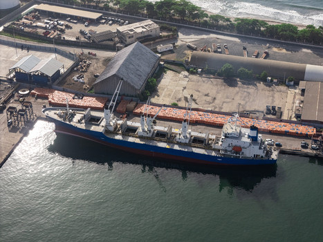 Aerial view of a cargo ship docked at the industrial port with stacks of orange cargo containers and warehouses nearby in Bajos de Haina San Cristobal Provinc Dominican Republic.