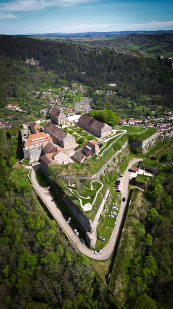 Aerial view of Fort Saint Andre with its historic stone walls and buildings surrounded by lush green forests under a clear blue sky Salins les Bains Bourgogne Franche Comte France. Aerial view of Fort Saint Andre with its historic stone walls and buildings surrounded by lush green forests under a clear blue sky Salins les Bains Bourgogne Franche Comte France.
