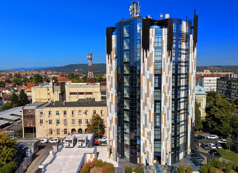 Aerial view of a modern cylindrical building with a glass and patterned facade in the city center surrounded by urban architecture and greenery in Krusevac Rasina District Serbia. Aerial view of a modern cylindrical building with a glass and patterned facade in the city center surrounded by urban architecture and greenery in Krusevac Rasina District Serbia.