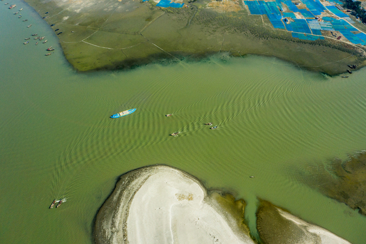 Aerial view of the coastal river landscape with small boats navigating near a sandbar in Kuakata Barisal Division Bangladesh. Aerial view of the coastal river landscape with small boats navigating near a sandbar in Kuakata Barisal Division Bangladesh.