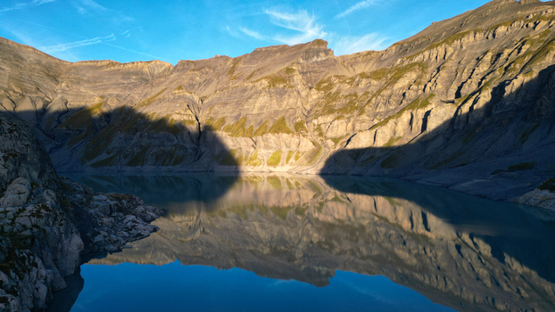 Aerial view of Vieux Emosson Lake and dam surrounded by rugged rocky peaks under a clear blue sky with calm water reflecting the dramatic landscape in Finhaut Valais Switzerland. Aerial view of Vieux Emosson Lake and dam surrounded by rugged rocky peaks under a clear blue sky with calm water reflecting the dramatic landscape in Finhaut Valais Switzerland.