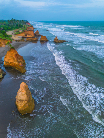 Aerial view of dramatic rock formations along the sandy coastline with crashing ocean waves and lush greenery in Bali Indonesia. Aerial view of dramatic rock formations along the sandy coastline with crashing ocean waves and lush greenery in Bali Indonesia.