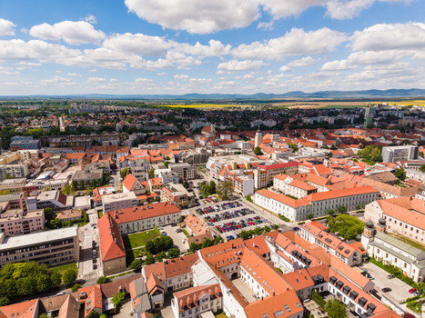 Aerial view of the historic city center with red rooftops church spires and a large parking lot under a blue sky with white clouds in Trnava Trnava Region Slovakia. Aerial view of the historic city center with red rooftops church spires and a large parking lot under a blue sky with white clouds in Trnava Trnava Region Slovakia.