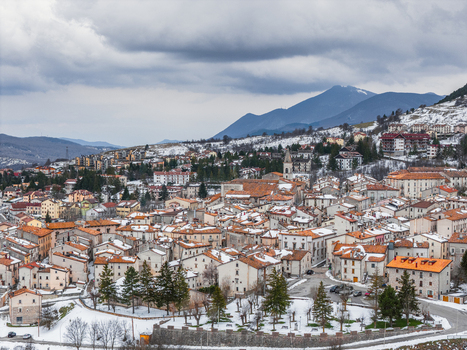 Aerial view of Pescocostanzo village with snow covered rooftops historic stone buildings and surrounding mountains under a cloudy sky in Pescocostanzo Abruzzo Italy.