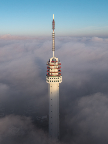 Aerial view of a tall communication tower rising above a thick layer of white clouds under a clear blue sky in Roermond Limburg Netherlands.