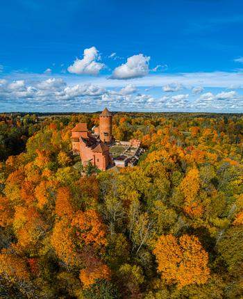 Aerial view of Turaida Castle surrounded by a vibrant autumn forest with colorful orange and yellow foliage under a clear blue sky in Sigulda Sigulda Municipality Latvia. Aerial view of Turaida Castle surrounded by a vibrant autumn forest with colorful orange and yellow foliage under a clear blue sky in Sigulda Sigulda Municipality Latvia.