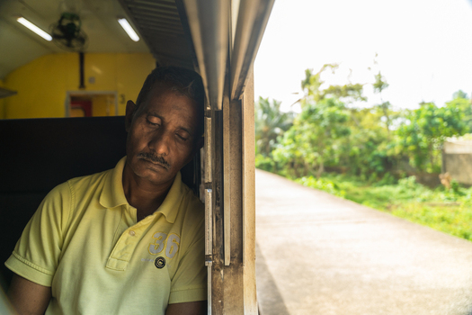Sri Lanka 06 February 2026 View of a man sleeping while leaning against a window inside a moving train passing through lush green landscapes.