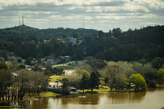 View of Lago del Fuerte surrounded by lush trees rolling hills and residential buildings under a cloudy sky in Tandil Provincia de Buenos Aires Argentina.