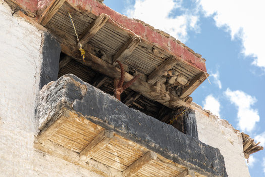 View of the traditional wooden balcony and weathered stone walls of Charasa Gonpa against a bright blue sky in Charasa Ladakh India.