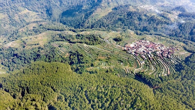 Aerial view of Keditan village nestled among lush green terraced rice fields and dense forest in the highlands of Central Java Ngablak Central Java Indonesia.