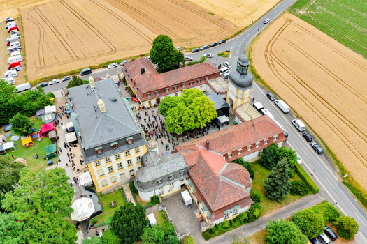 Aerial view of Schloss Jagersburg featuring its historic architecture a courtyard filled with people and surrounding agricultural fields in Eggolsheim Bayern Germany. Aerial view of Schloss Jagersburg featuring its historic architecture a courtyard filled with people and surrounding agricultural fields in Eggolsheim Bayern Germany.