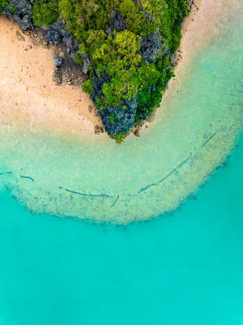 Aerial view of a rocky limestone karst formation covered in lush green vegetation meeting a sandy beach and turquoise coastal waters in Vietnam. Aerial view of a rocky limestone karst formation covered in lush green vegetation meeting a sandy beach and turquoise coastal waters in Vietnam.