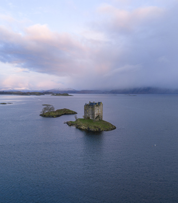 Aerial view of Castle Stalker on a small tidal islet surrounded by the calm waters of Loch Laich under a soft cloudy sky Appin Scotland United Kingdom. Aerial view of Castle Stalker on a small tidal islet surrounded by the calm waters of Loch Laich under a soft cloudy sky Appin Scotland United Kingdom.