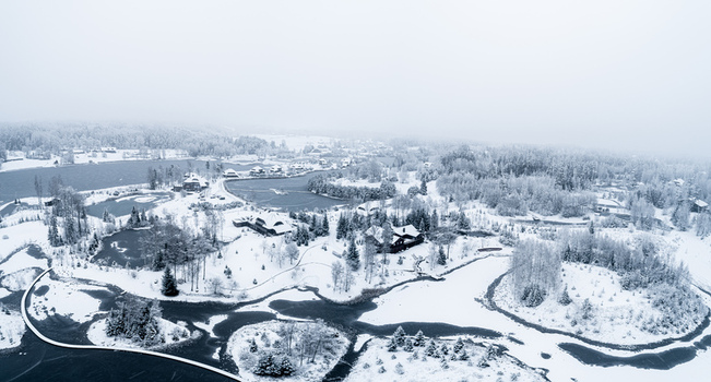 Aerial view of a snow covered landscape featuring frozen ponds scattered wooden houses and dense pine forests under a winter sky in Latvia. Aerial view of a snow covered landscape featuring frozen ponds scattered wooden houses and dense pine forests under a winter sky in Latvia.