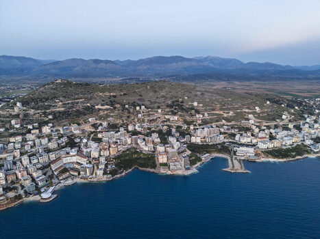 Aerial view of dense urban development and buildings stretching along the Ionian Sea coastline set against rolling hills in Saranda Vlore County Albania. Aerial view of dense urban development and buildings stretching along the Ionian Sea coastline set against rolling hills in Saranda Vlore County Albania.