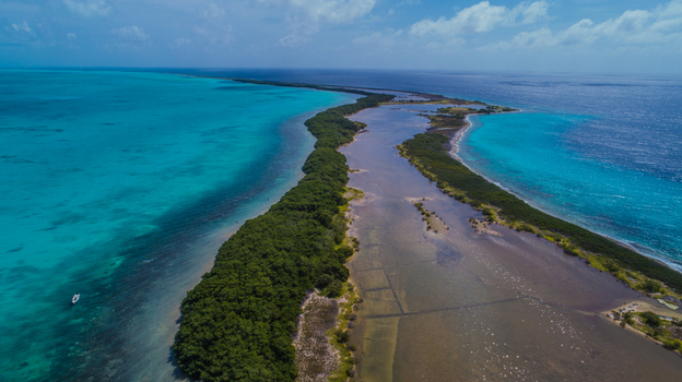 Aerial view of Los Roques archipelago featuring lush mangroves shallow turquoise waters and a small boat in the Caribbean Sea Los Roques Dependencias Federales Venezuela. Aerial view of Los Roques archipelago featuring lush mangroves shallow turquoise waters and a small boat in the Caribbean Sea Los Roques Dependencias Federales Venezuela.