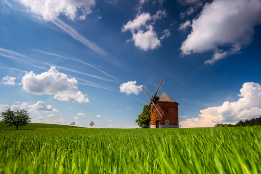 View of a historic brick windmill standing in a vibrant green field under a bright blue sky with fluffy white clouds in Brno City District South Moravian Region Czechia.