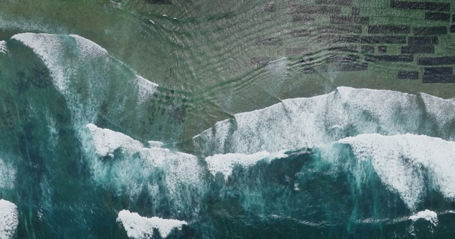 Aerial view of turquoise ocean waves crashing over a shallow reef with white sea foam patterns in Lombok West Nusa Tenggara Indonesia.