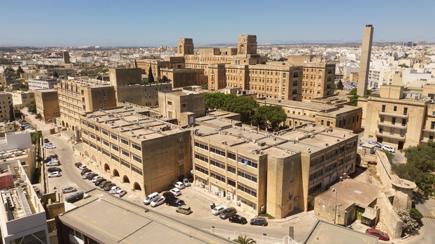 Aerial view of the historic St. Luke s Hospital complex with its limestone architecture and flat roofs surrounded by urban streets and parking areas in Valletta Port Region Malta. Aerial view of the historic St. Luke s Hospital complex with its limestone architecture and flat roofs surrounded by urban streets and parking areas in Valletta Port Region Malta.