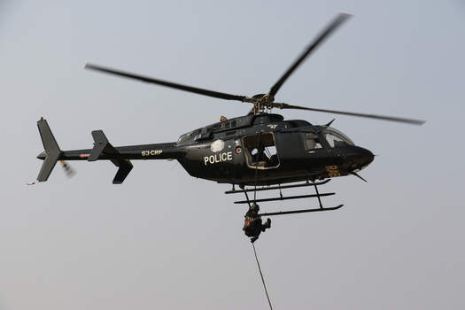 Dhaka Bangladesh 01 February 2017 View of a black police helicopter in flight with a Rapid Action Battalion officer rappelling from a rope against a clear sky. Dhaka Bangladesh 01 February 2017 View of a black police helicopter in flight with a Rapid Action Battalion officer rappelling from a rope against a clear sky.