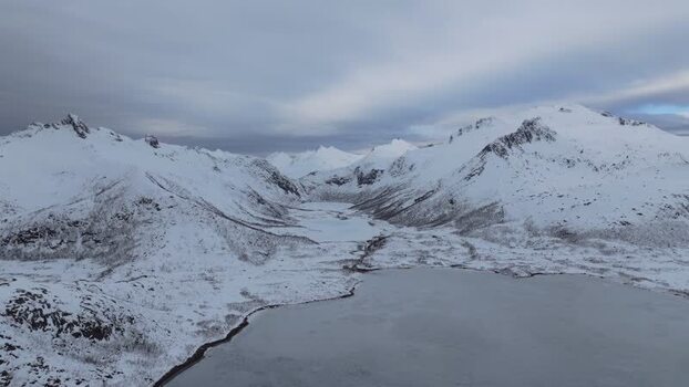 Aerial view of snowy mountains and frozen lake in Lofoten Norway.