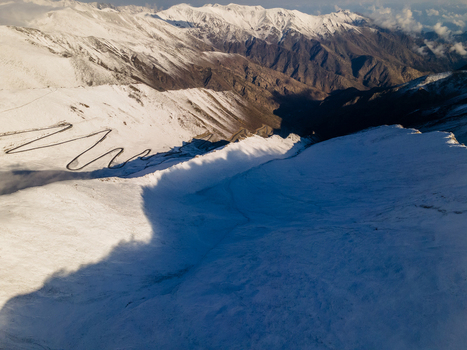 Aerial view of the winding road of Babusar Pass through snow covered mountain peaks under bright sunlight in Babusar KPK Pakistan.