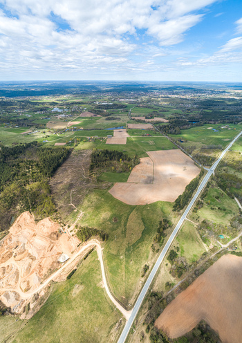 Aerial view of a rural landscape featuring agricultural fields patches of forest a winding road and a sand quarry under a blue sky with scattered clouds Latvia. Aerial view of a rural landscape featuring agricultural fields patches of forest a winding road and a sand quarry under a blue sky with scattered clouds Latvia.